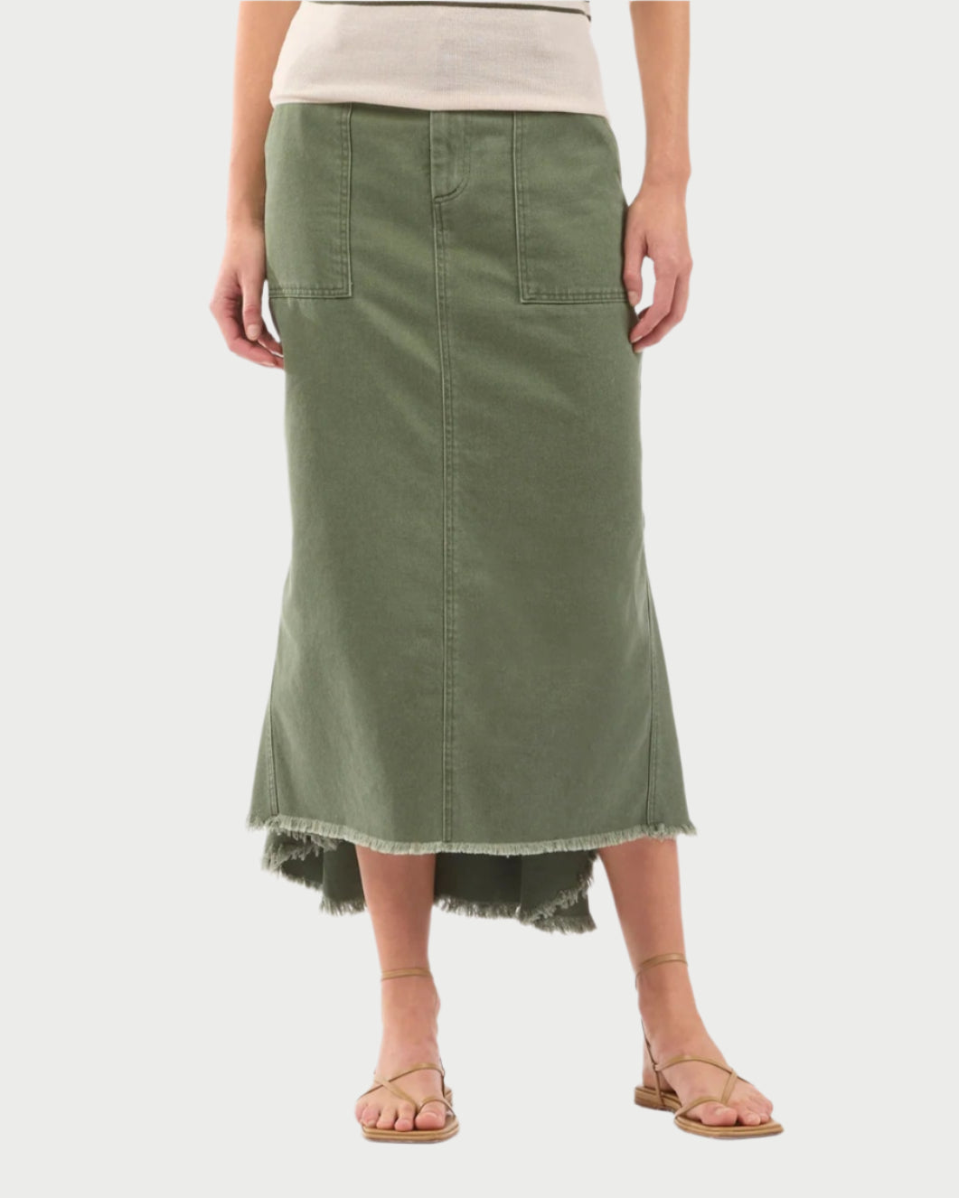 A person wearing Le Superbe's Very Mindful Skirt, a vintage-inspired long green skirt with a frayed hem and large cargo-style pockets, paired with a white top and brown sandals against a plain white background.