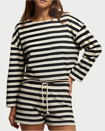 A person poses with a hand on their hip, wearing the Taylor Striped Cotton Tee by perfectwhitetee and matching shorts. The black and white set features horizontal stripes, long sleeves, a drawstring waist, and is made from recycled cotton.