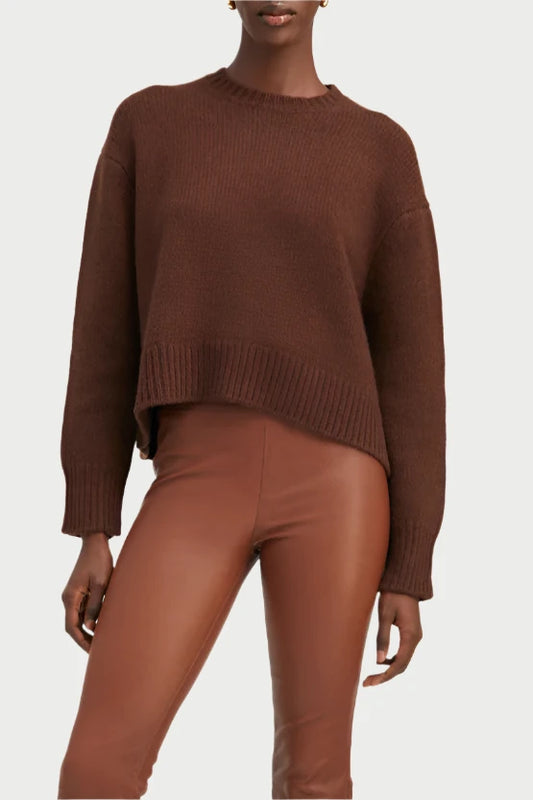 A person is posed confidently against a plain backdrop, dressed in a brown SPRWMN Heavy Crewneck Sweater paired with brown leather pants and black heeled boots. Their poised stance, highlighted by one hand resting casually at their side, makes this ensemble perfect for fall.