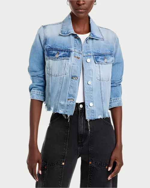 A person wearing Frame's Vintage Denim Distressed Jacket with a frayed hem over a white top. The stylish jacket features button closures and two chest pockets. They are also sporting high-waisted black jeans with pockets and seams. The sleeves of the jacket are rolled up to the elbows.