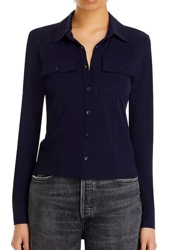 A person wearing a dark blue, long-sleeve Frame Jersey Button Up Shirt with two button flap pockets, paired with high-waisted dark gray jeans. The shirt has a collar and is buttoned halfway down. The image is cropped at the shoulders and mid-thigh, showcasing the quality craftsmanship in every detail.