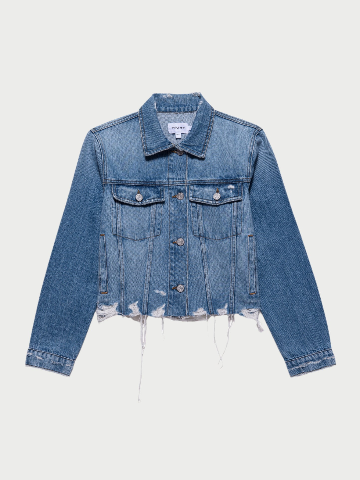 A stylish "Vintage Denim Distressed Jacket" by Frame with long sleeves and a distressed, frayed hem. This vintage denim jacket features two buttoned chest pockets, buttoned cuffs, and a collared neckline. Its slightly faded appearance enhances its timeless look.