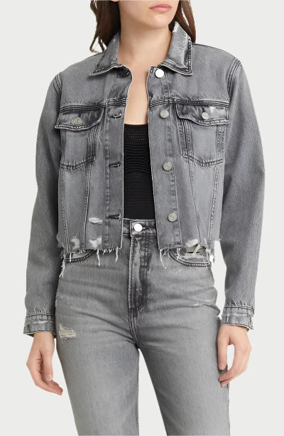 A person stands wearing Frame's Distressed Denim Jacket, featuring a vintage-style and frayed hem in a light-gray hue, paired with matching high-waisted gray jeans and a vintage black top. Perfect for Spring, Summer, or Fall, the image focuses on the clothing, with the person's face not visible.