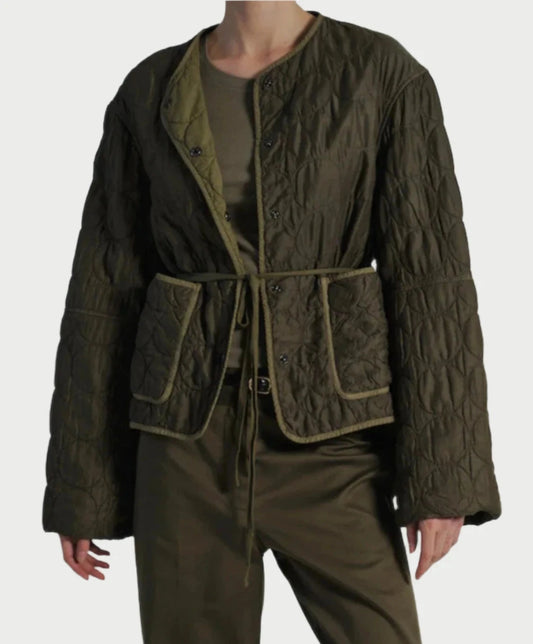 A person is sporting a dark green Quilted Jacket by Saint Art NY, complete with a tie belt over an olive green shirt and matching olive green pants. The jacket showcases a textured pattern and front pockets. This casual, monochromatic ensemble exudes a modern vibe, thanks to its garment-dyed finish.