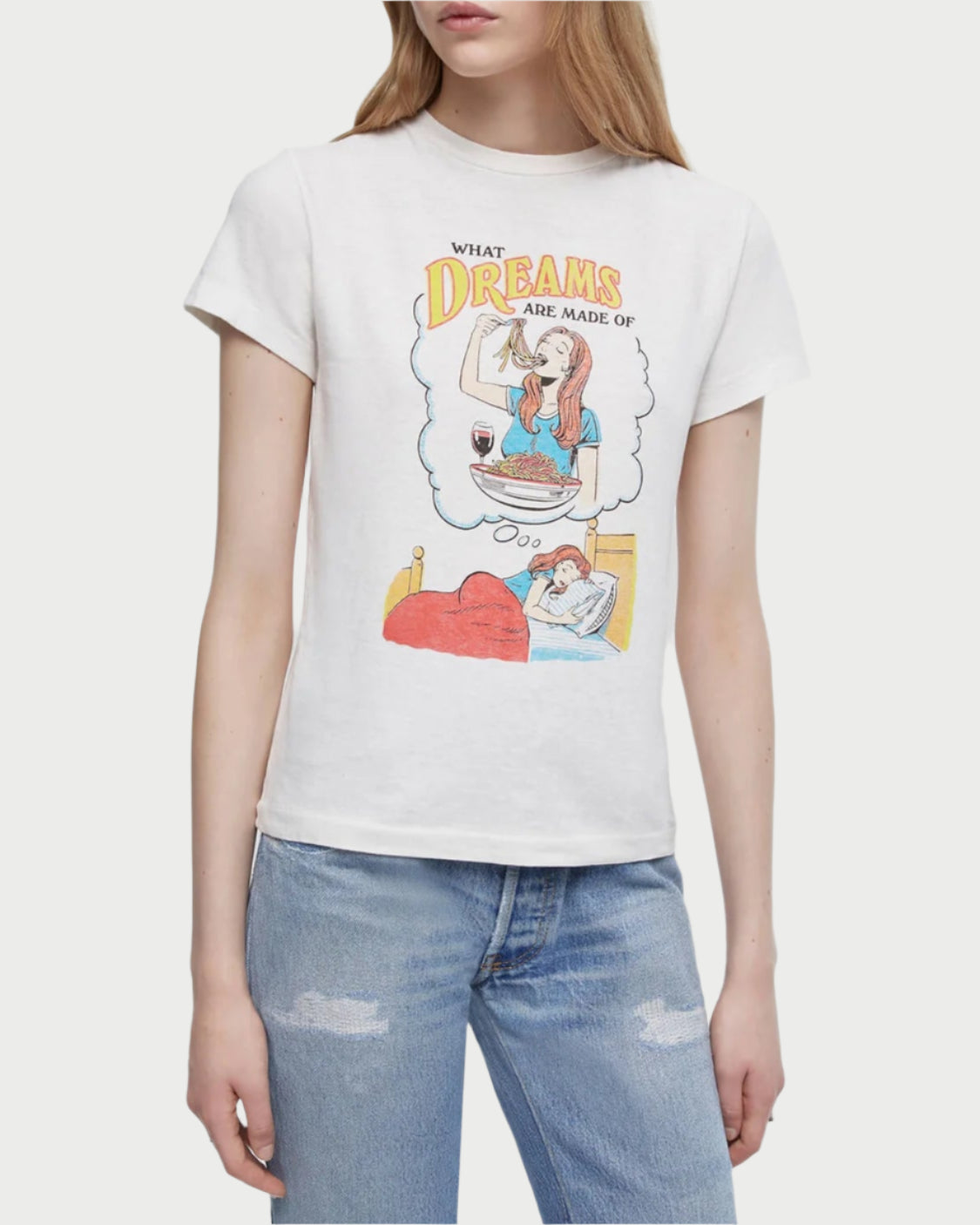 A woman wears a white RE/DONE Dreams Classic Tee with a vintage-inspired graphic of someone dreaming of pizza and wine, featuring the text "What dreams are made of." She pairs it effortlessly with light blue jeans.