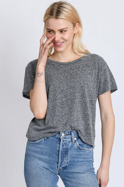 A person with long blonde hair and a small tattoo on their forearm smiles while wearing a Perfectwhitetee Harley Boxy Crew in Multiple Colors layered stylishly over a gray T-shirt, complemented by blue jeans. They touch their face with one hand against a light-colored background, adding multiple colors to the subtle scene.