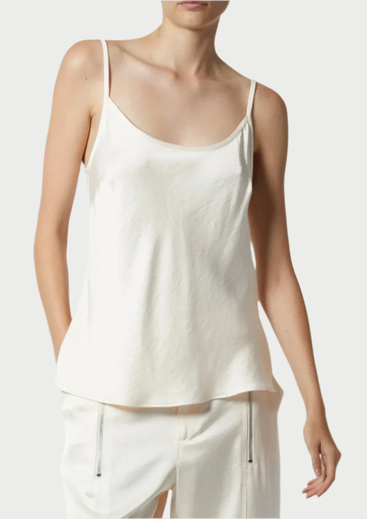 A person wearing a Saint Art NY Charmeuse Cami, a white, sleeveless camisole with thin straps, paired with white pants featuring zipper details. The silky-smooth fabric exudes modern femininity. Only the upper body is visible against a plain background, highlighting the simple, casual style of the outfit.