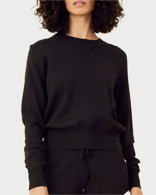 A person is wearing the Warwick Cotton Pullover by One Grey Day, paired with matching pants. They have curly dark hair, and their face is partially obscured against a plain light background.