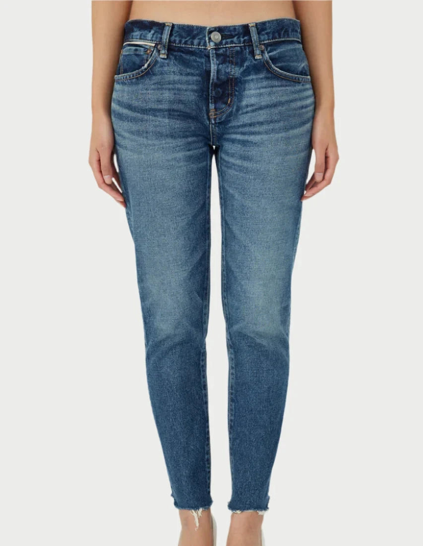 A person wearing Moussy's Ivanhoe Tapered Mid Rise Jeans, crafted from premium Japanese denim, stands against a plain background. These jeans offer a flattering fit with a button and zipper closure, front pockets, and slightly frayed hems at the ankles.