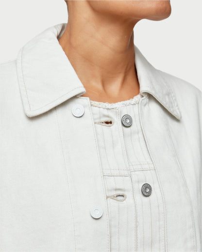 A close-up shows a person wearing the off-white Hanson Layered Jacket by Moussy over a textured shirt. Ideal for spring, it has a pointed collar, button details, and visible stitching as the person’s chin and neck slightly turn away from the camera.