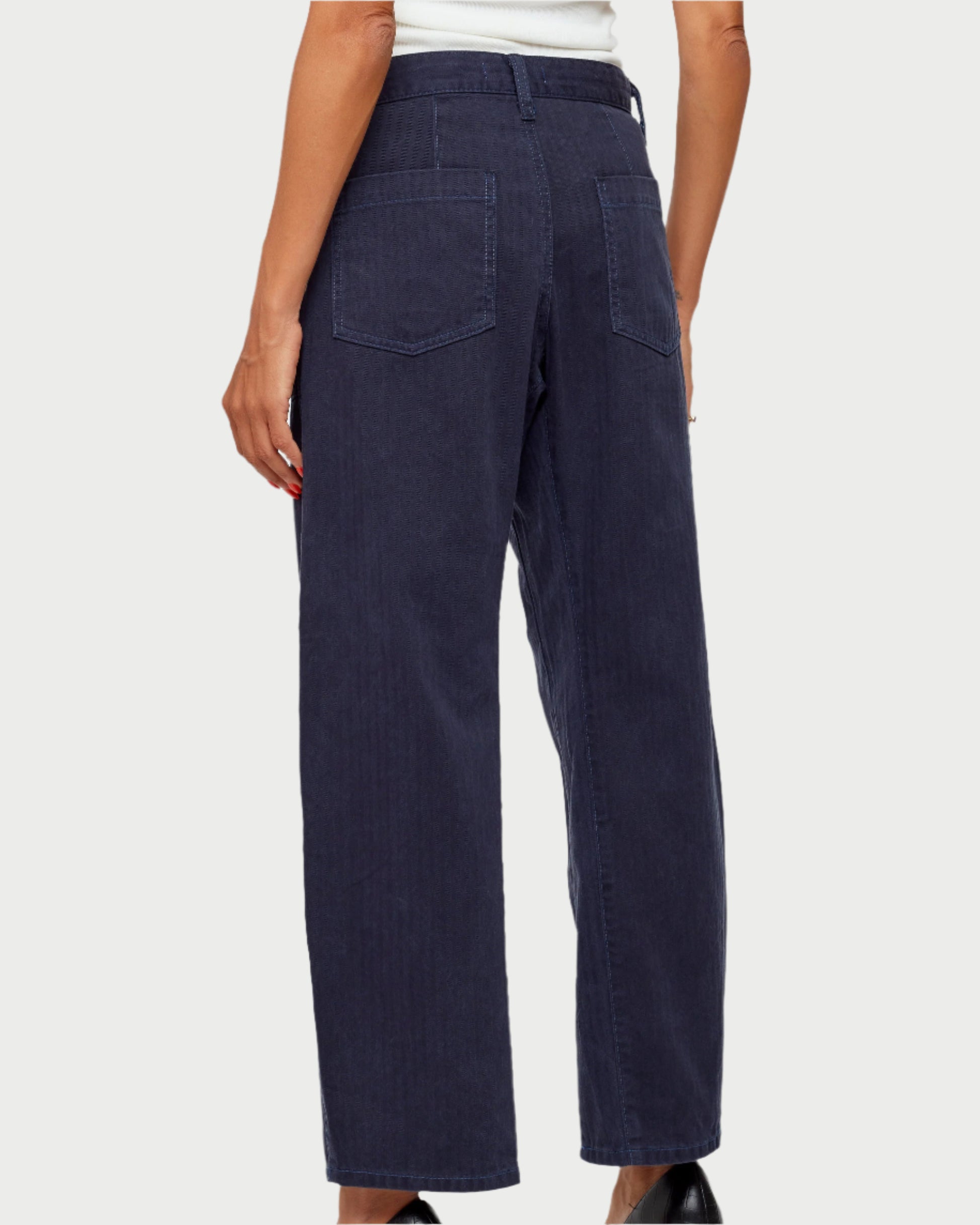 Wearing Moussy's Crotona Cargo Pants in dark blue, a person stands with their back to the camera, large back pockets visible. They pair it with a white top and black shoes against a light gray backdrop.