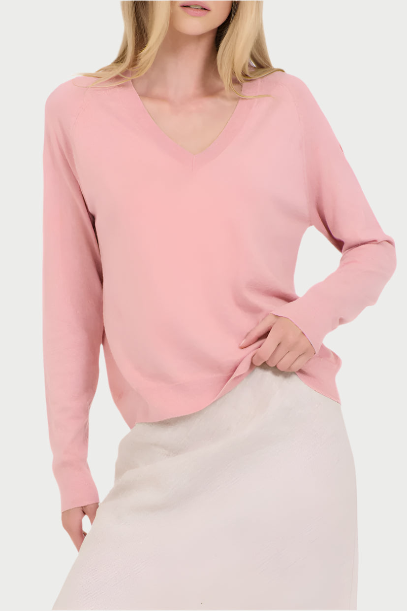 Wearing a Sloane Cotton V-Neck Sweater by One Grey Day and a light-colored skirt, the person stands with one hand on their hip. The image captures a casual, relaxed pose against a pristine white background, highlighting this feminine essential with effortless elegance.