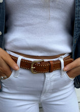 Load image into Gallery viewer, A person wearing a white ribbed shirt tucked into white jeans with a studded brown leather Frame Belt from Frame. Their hands are tucked into the jeans&#39; pockets, and a denim jacket can be seen on their sides. Gold rings are visible on their fingers.
