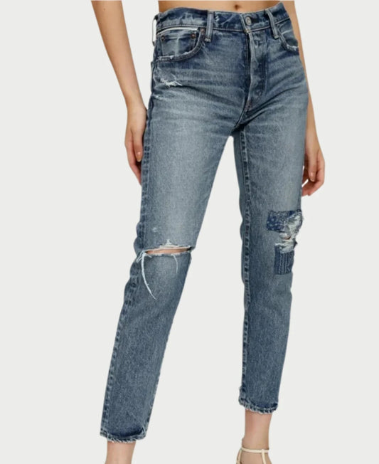 A person wearing the Monroe Tapered Jeans by Moussy, featuring high-waisted design, patchwork details, and fraying on one knee from a unique denim collection, stands against a neutral background.