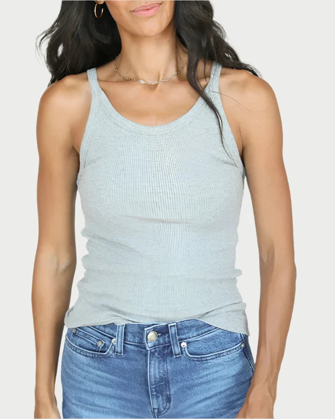 A woman with long, wavy dark hair stands against a white background. She is wearing the perfectwhitetee Annie Tank and blue jeans. She has a neutral expression on her face and her arms are relaxed by her sides. She has hoop earrings and a thin necklace.