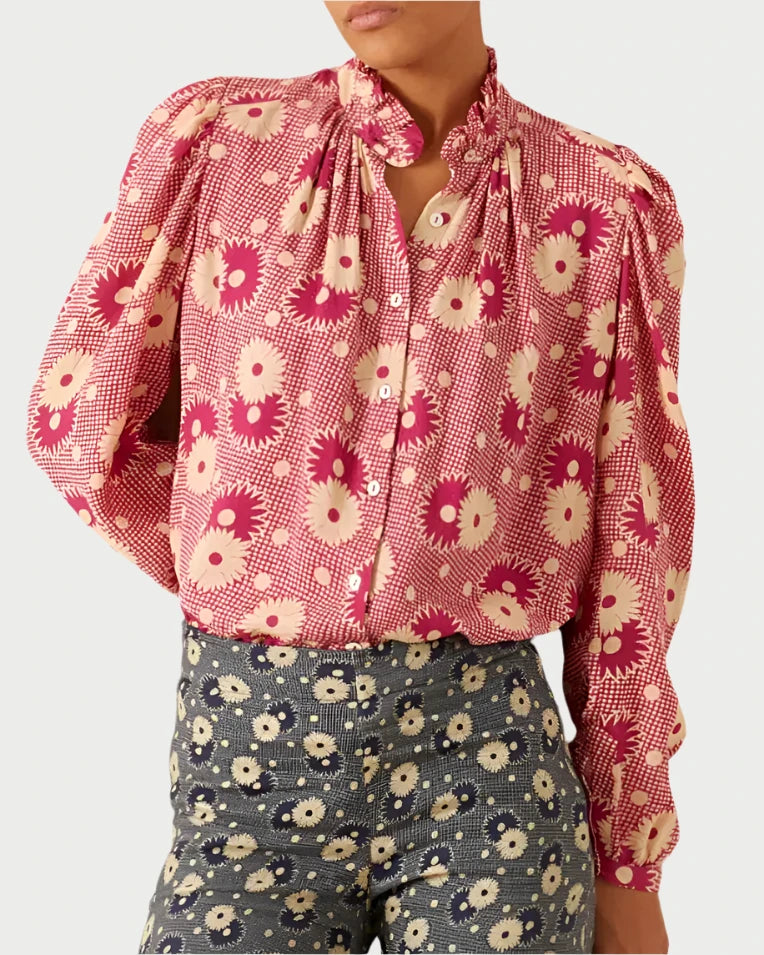 A person wearing the Annabel Berry Daisy Shirt by Alix of Bohemia, featuring a retro style with large floral patterns in pink, paired with high-waisted blue pants that have smaller floral designs.