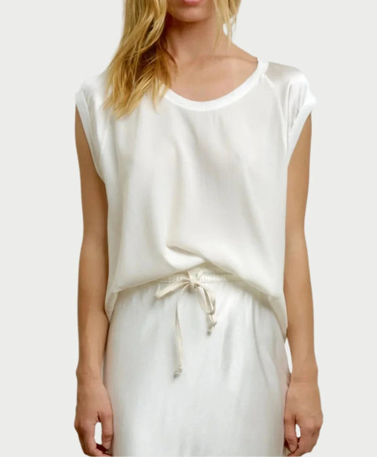 A person with long, blonde hair is wearing the Cap Sleeve Silk Baseball Tee in Cloud by AqC, featuring a loose fit, short sleeves, a drawstring waist, and shiny sleeves. The background is a plain, light color.