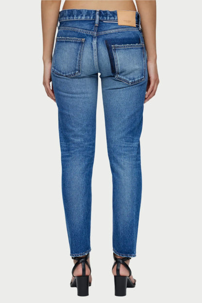 A person is seen from the back wearing high-waisted Forestville Tapered Jeans from Moussy, featuring a leather patch. The jeans have a faded wash with slight distressing and are paired with strappy black heeled sandals against a plain, light background.