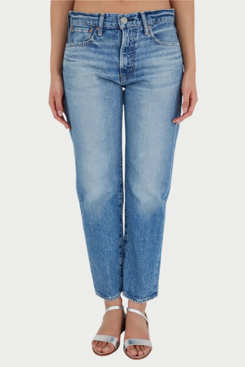 A person is wearing light blue, high-waisted MAPLECREST BOYS JEANS by Moussy and silver ankle-strap sandals. Their arms are not visible in the frame, and they are standing against a plain white background. The cropped length of the jeans adds a chic touch to their outfit.