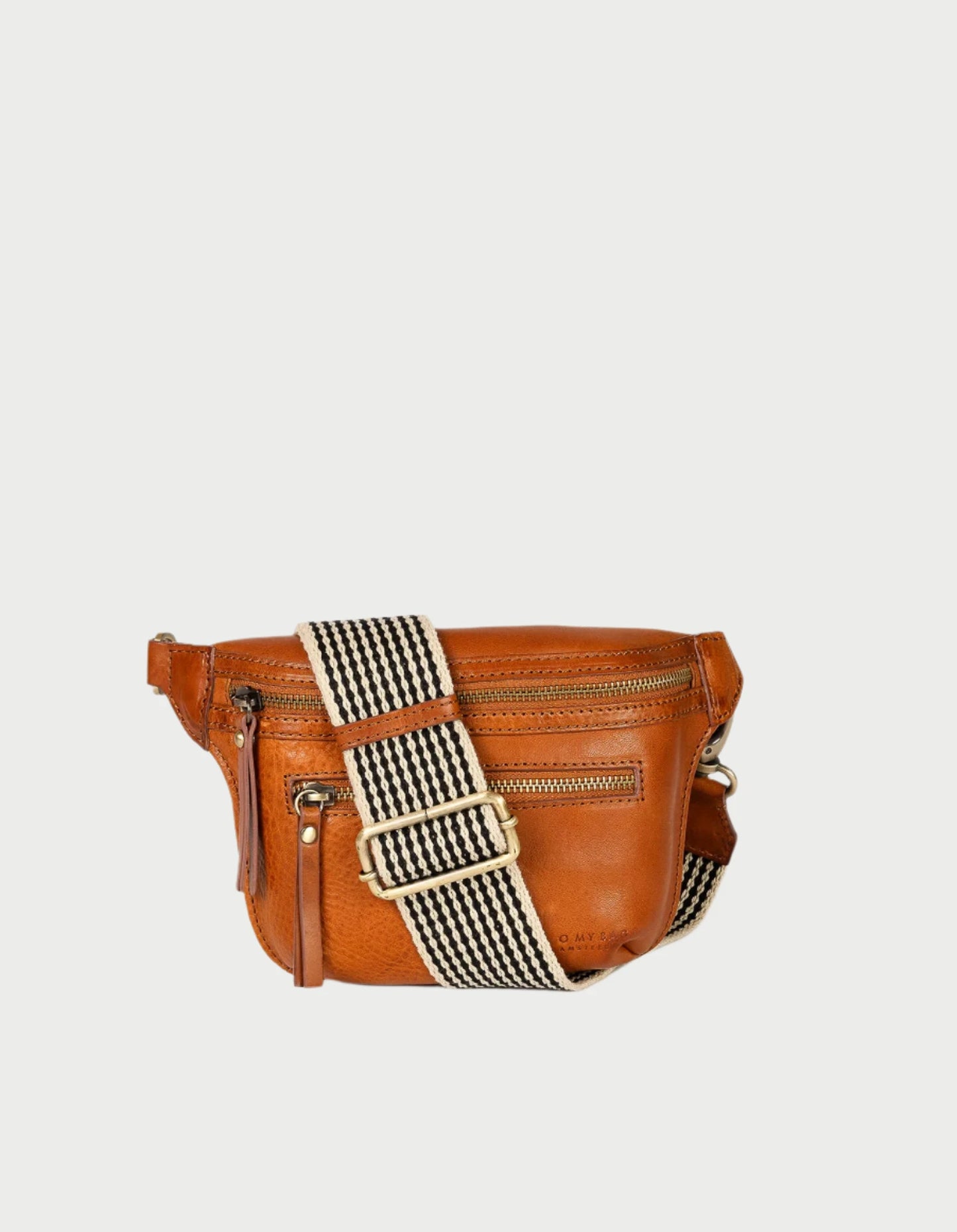 Introducing the Beck's Bum Bag in Cognac by O MY BAG, a stylish brown leather crossbody with a striped adjustable strap. This sleek design merges practicality and fashion, featuring two zippered compartments for convenience.