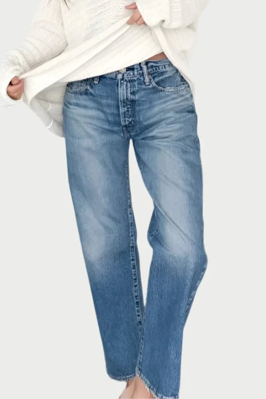 A person wearing a loose white sweater and MAPLECREST BOYS JEANS by Moussy stands barefoot against a plain white background. They are slightly bent forward, looking down and holding the edge of their sweater with one hand.