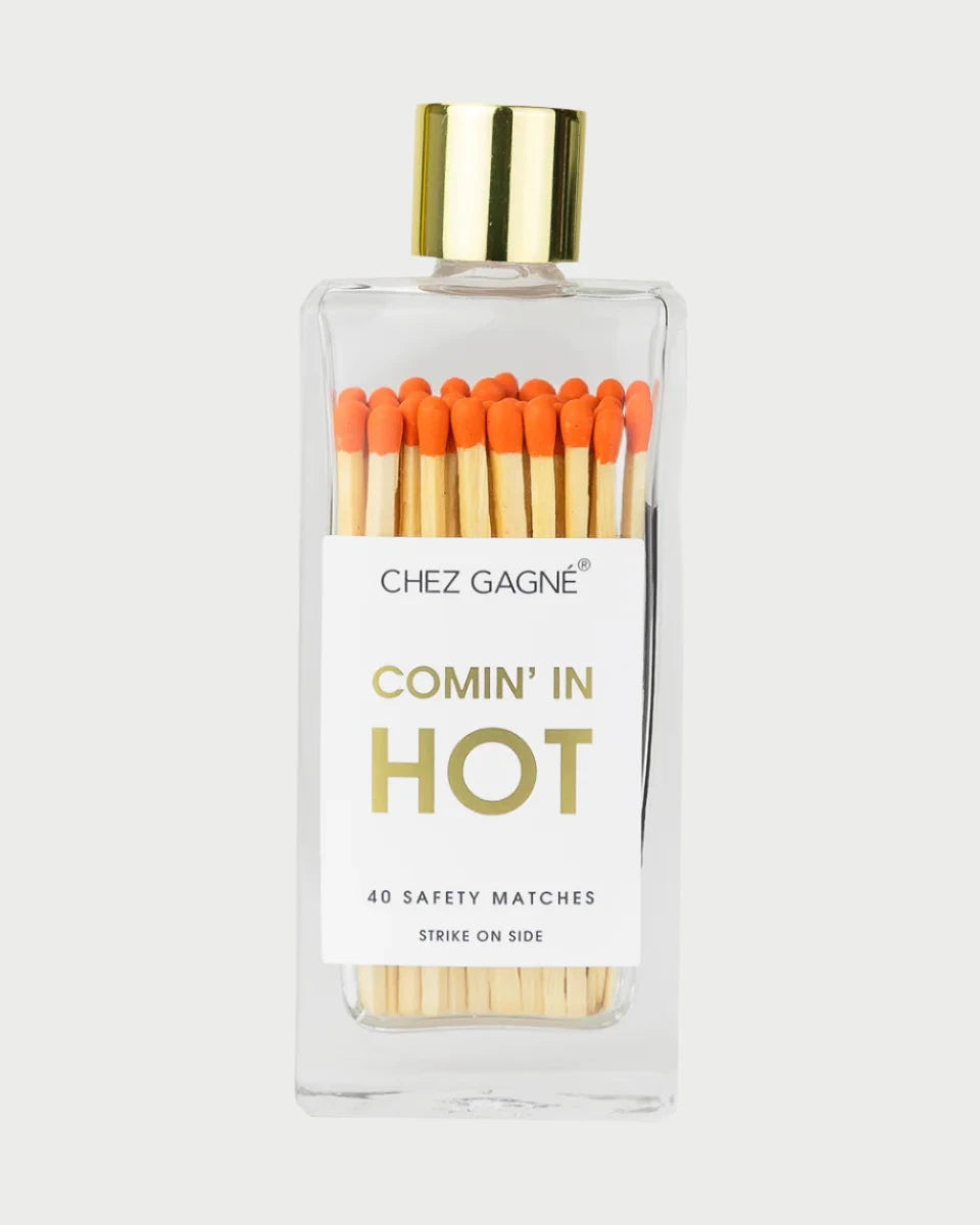 A transparent bottle topped with a gold cap contains vibrant matches featuring orange tips, adorned with a label that says "Chez Gagné, Comin' in Hot, 40 Safety Matches, Strike on Side.