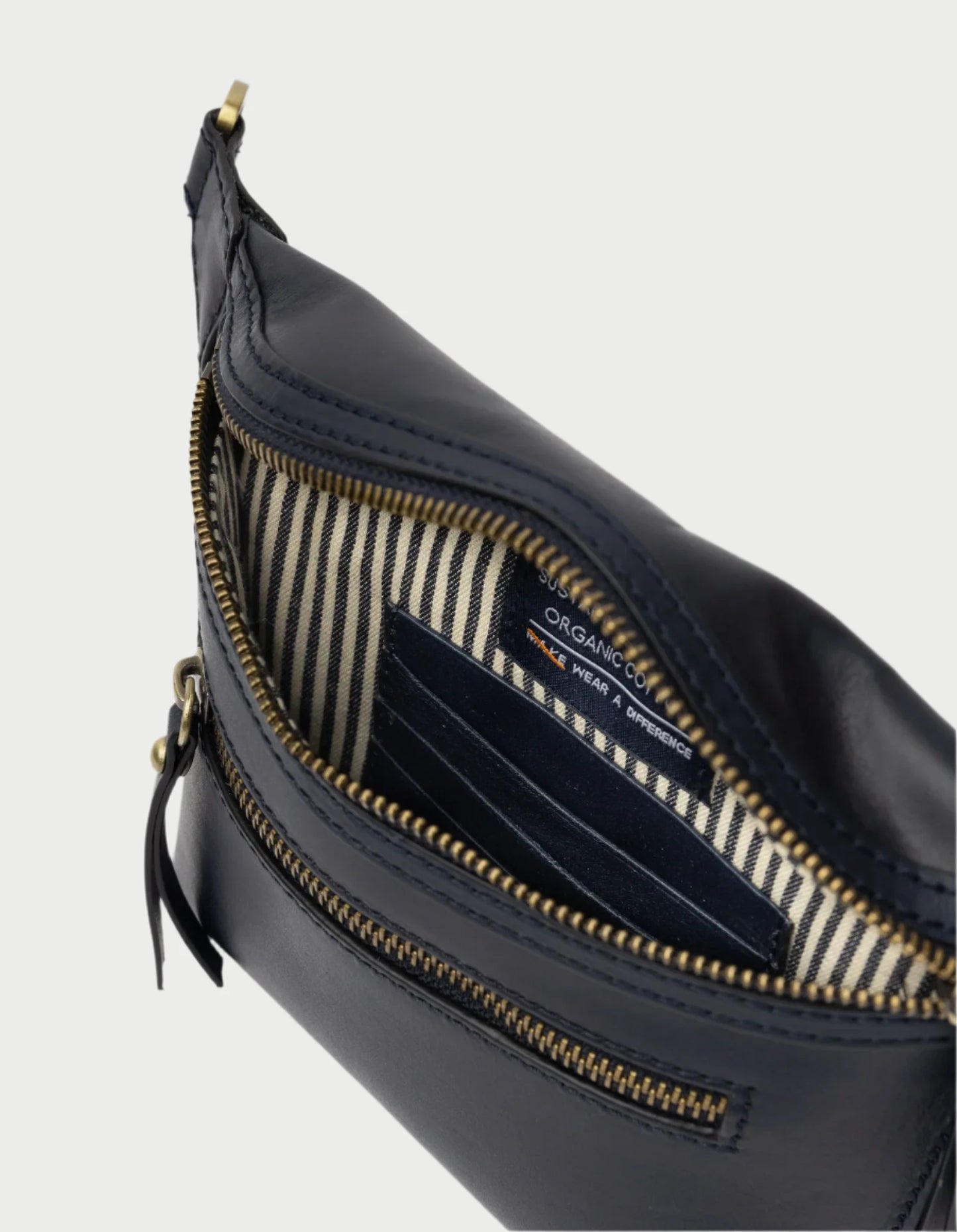 Unzip the midnight blue Beck's Bum Bag by O MY BAG to reveal a striped fabric interior reminiscent of a chic crossbody design. The bag features card slots and a label indicating "organic content." Gold zipper details add elegance to this stylish accessory.