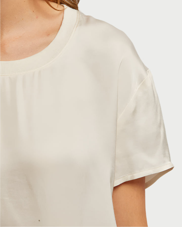 Close-up of a person wearing the Delphine Satin Crewneck Tee from perfect white tee: light beige crewneck made of 100% viscose. The image focuses on the left shoulder and upper chest, highlighting the short sleeve and round neckline against a plain background.