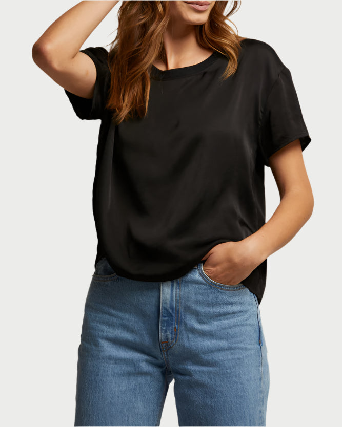 A person in a Delphine Satin Crewneck Tee by perfect white tee and blue jeans stands with one hand on their hip, the other arm raised, slightly tilting their head. The outfit is an elevated essential, blending casual style with sophistication.