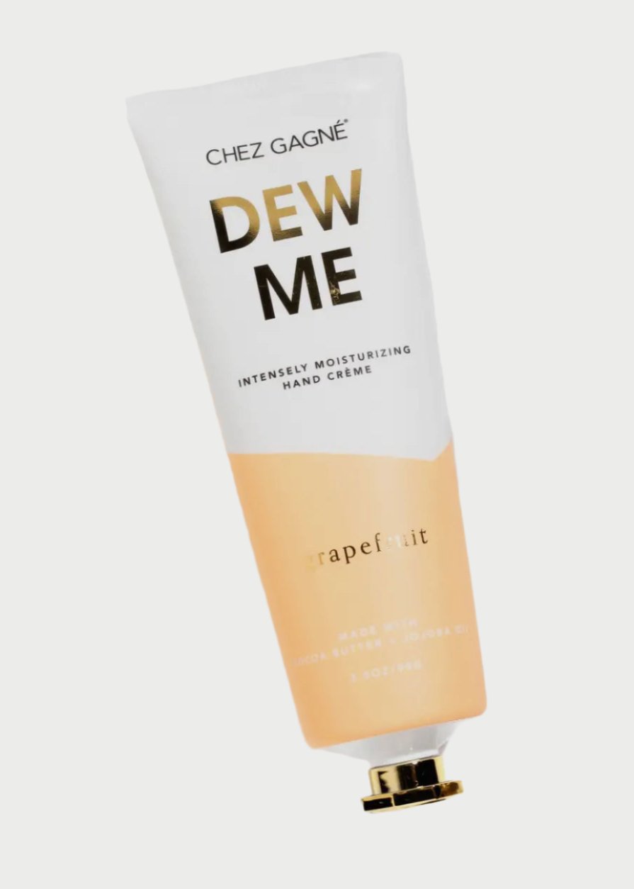 A white and peach-colored tube of Chez Gagné's Hand Creme in grapefruit scent. The tube, enriched with Jojoba Oil and Cocoa Butter, has gold accents and is laying on a white background. The cap is off and placed next to the tube.