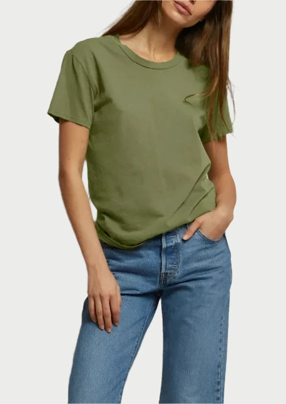 A woman with long brown hair is wearing the versatile and comfortable Harley Tee Safari by perfectwhitetee paired with blue jeans. She stands against a light-colored background, one hand in her pocket and the other hanging down at her side.