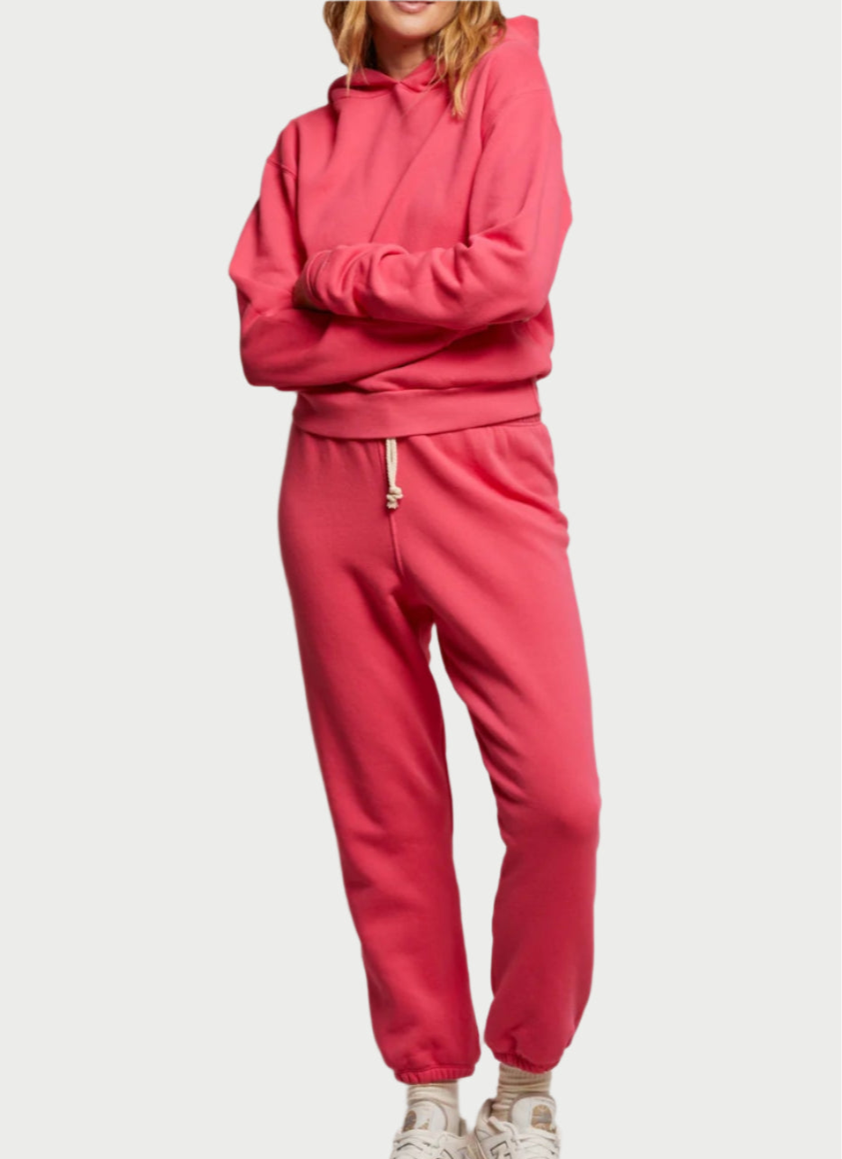 A person in a Pink Bloom hoodie and Stevie Sweatpant by perfectwhitetee stands with crossed arms. With long hair and white sneakers, they showcase a casual, stylish look in cozy cotton fleece against a plain white background.