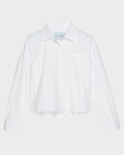 The T. Line Coco Cropped Shirt is a chic white long-sleeved button-up, featuring a stylish chest pocket and pointed collar. Made from 100% cotton, it stands gracefully against a light gray background.