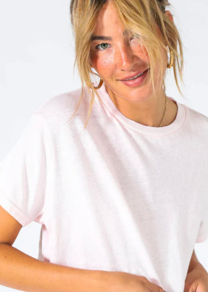 A person with blonde hair tied in a loose ponytail and bangs is wearing the Harley Boxy Crew in Multiple Colors by perfectwhitetee that's perfect as a layering piece, paired with gold hoops. They are tilting their head slightly and smiling against a plain white background.