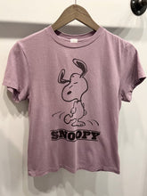 Load image into Gallery viewer, A relaxed fit purple Snoopy Dancing Classic Tee by RE/DONE on a wooden hanger, featuring a black line drawing of Snoopy, the beloved cartoon character from the Peanuts comic strip, in a sassy pose with eyes closed and ears up. The text &quot;SNOOPY&quot; is printed below the vintage-inspired drawing.