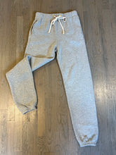 Load image into Gallery viewer, A pair of Dylan Classic Sweatpants by Les Tien in gray with a white drawstring is laid out on a wooden floor. The sweatpants feature side pockets and elasticized cuffs at the ankles, offering an elevated look.