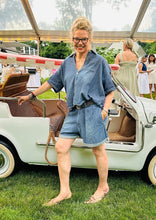Load image into Gallery viewer, A person with blonde hair wearing a blue romper and glasses stands beside a small, vintage, white convertible car. The car is equipped with a rope instead of a standard door handle. There is a gathering of people in the background under a large, clear tent, making the Double Pleat Shorts by Denimist feel like an essential part of any Spring/Summer wardrobe.