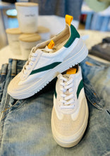 Load image into Gallery viewer, A pair of stylish Oncept Lagos Shoes with vibrant green accents and yellow pull tabs are displayed on top of a pair of blue jeans. In the background, several coffee cups and blurred objects enhance the contemporary style of the scene.