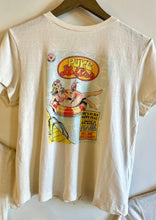 Load image into Gallery viewer, A RE/DONE Pure Bliss Classic Tee made of 100% cotton, featuring a colorful graphic of a woman lounging in a pool float with the text &quot;Pure Bliss&quot; in a stylized font. Additional text reads: &quot;She&#39;s in her happy place again...will she ever leave?&quot; The shirt is hung on a wooden hanger.