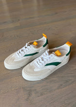 Load image into Gallery viewer, A pair of Lagos Shoes by Oncept in a contemporary style, featuring vibrant green detailing on the sides and orange pull tabs on the back, are placed on a wooden floor. The white shoes have matching laces and perforated toe boxes.