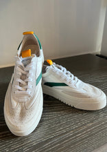 Load image into Gallery viewer, A pair of white leather Oncept Lagos Shoes with vibrant green and yellow accents displayed on a wooden surface. The shoes have white laces, perforated toe boxes for ventilation, and sturdy white soles with a grooved pattern for grip, embodying a contemporary style.