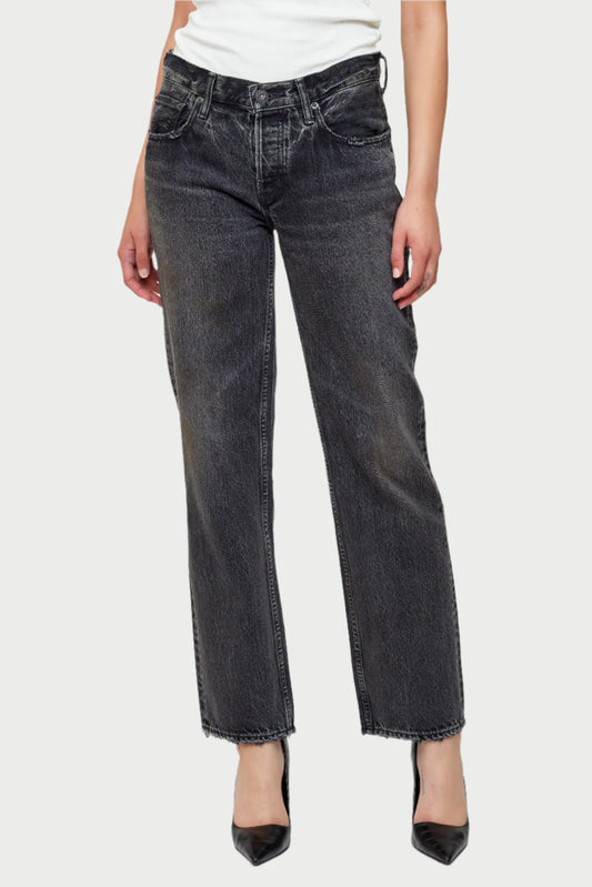 A person is dressed in Moussy Iona Straight Jeans, featuring non-stretch denim and frayed hems, paired with a white top and set against a plain background. The look is finished with black pointed-toe shoes.