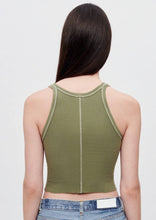 Load image into Gallery viewer, A person with long, dark hair is seen from the back, wearing an olive green Cropped Rib Bayleaf Tank by RE/DONE with visible stitching and a racerback sleeveless design. They are also wearing blue jeans with a white label on the waistband. The background is plain and light-colored.