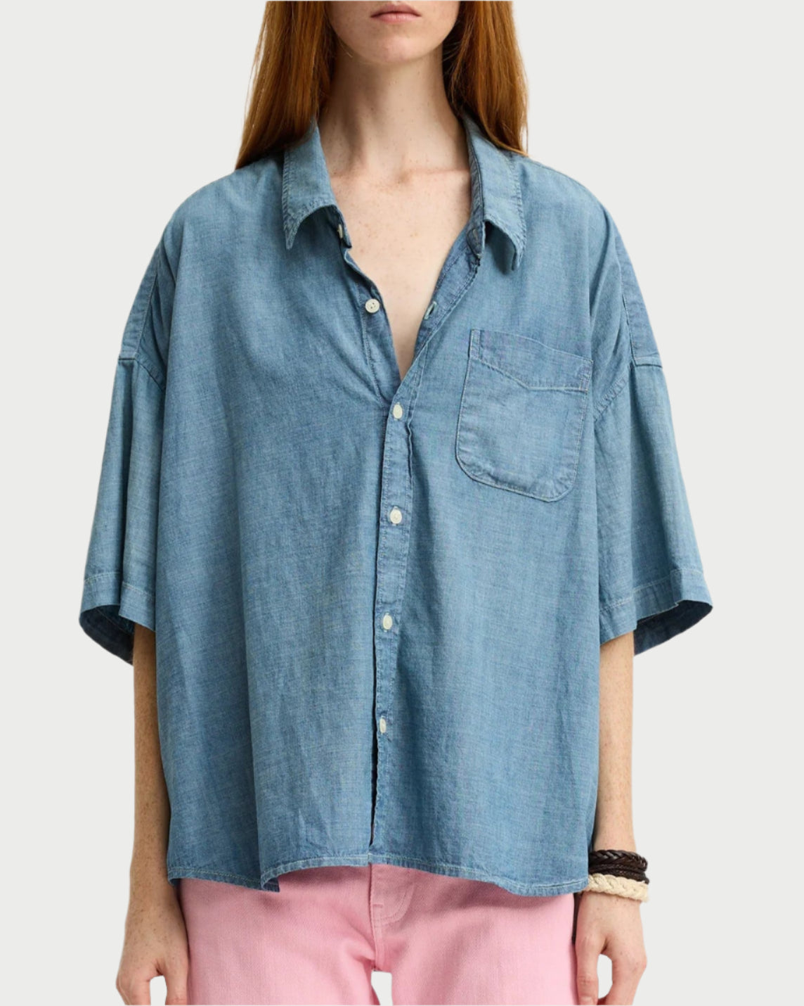 Wearing a Denimist SS Denim Shirt, made from 100% cotton with a chest pocket, and styled with light pink pants, a person with long brown hair stands against a plain light background.