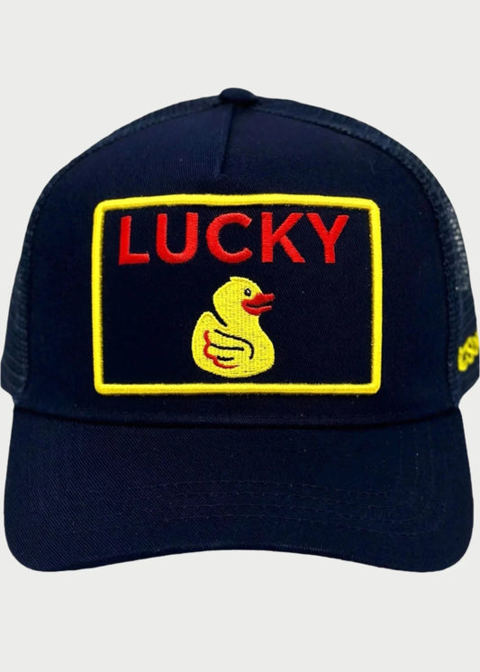 The Soulbyrd Lucky Duck Trucker Hat is a black cap featuring a front rectangular patch adorned with an illustration of a yellow duck and the phrase "LUCKY DUCK" in red letters above it. The hat includes a yellow detail on the side and has a breathable mesh back, making it ideal for individuals seeking to attract positive vibes.