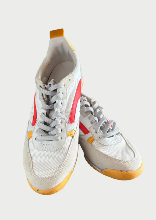 A pair of Oncept Montreal Shoe with white uppers, red accents, and yellow soles is displayed on a wooden surface. The shoes have grey laces and appear brand new. They exude effortless style with their sleek design and modern look.