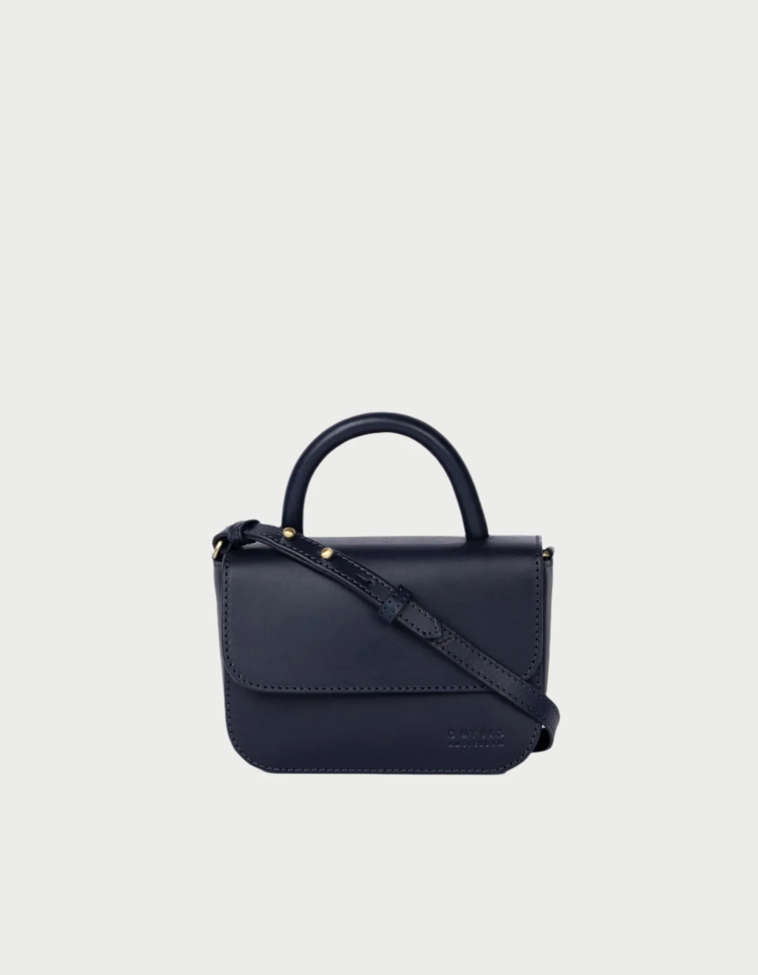 O MY BAG's Nano Bag is a chic, small black leather accessory featuring a top handle, detachable crossbody strap, and flap closure. Displayed against a plain background, its design is simple yet elegant.