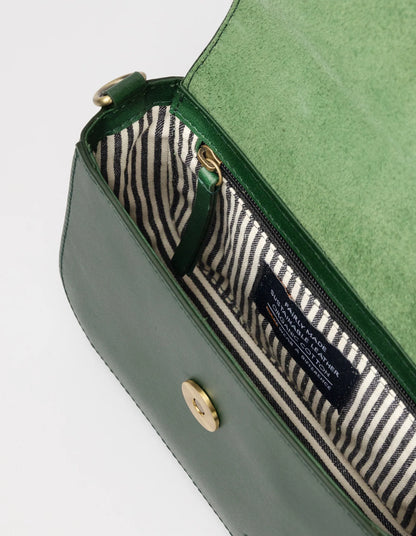 The green handbag, reminiscent of a chic Nano Bag by O MY BAG, features a magnetic clasp, revealing a black-and-white striped interior with a zip pocket. Its rectangular shape, smooth texture, gold hardware accents, and adjustable crossbody strap offer versatile wear.