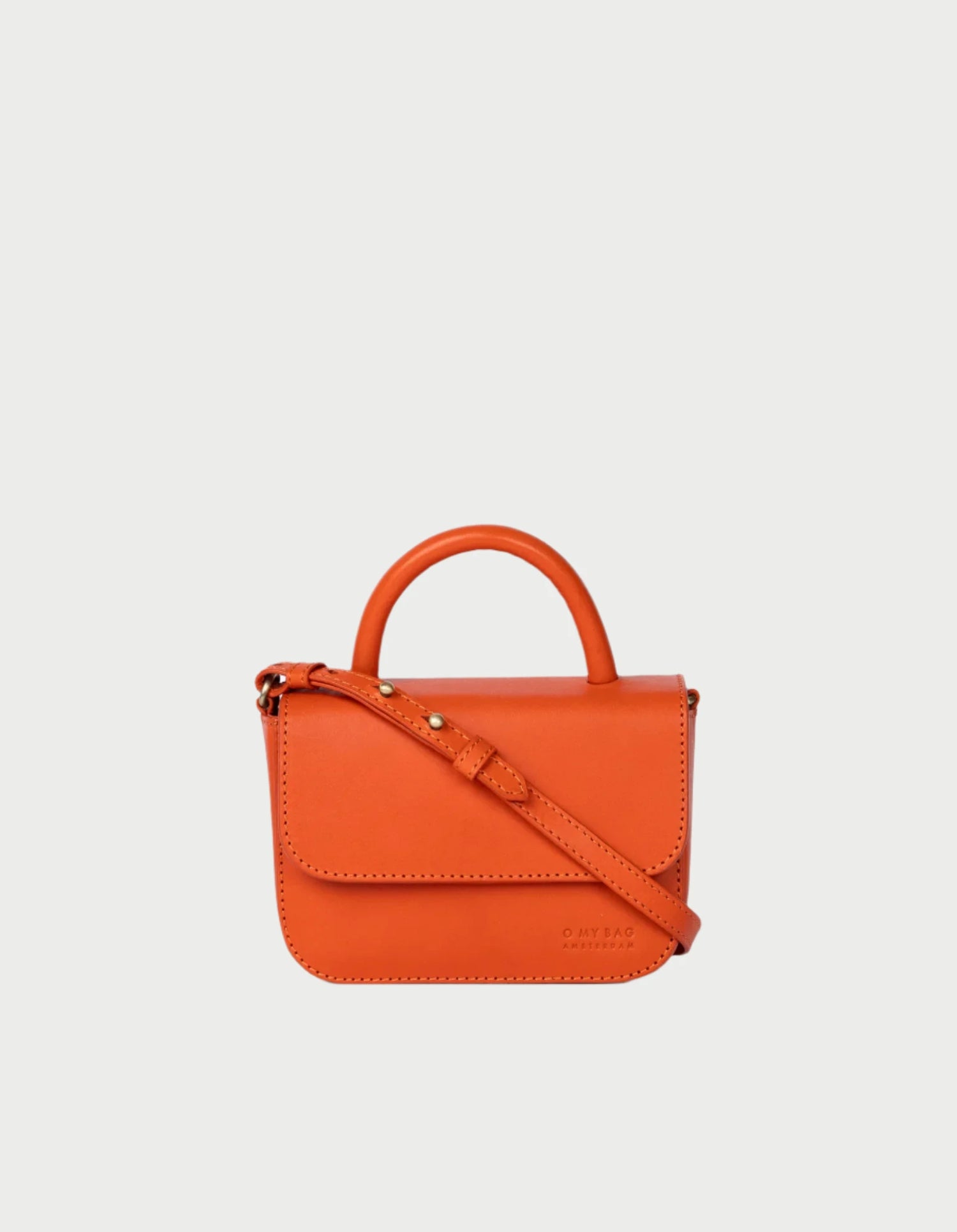 The Nano Bag in Orange by O MY BAG, celebrated for its adorable design, includes both a handle and an adjustable shoulder strap. It showcases a front flap with minimal stitching on a plain white background.