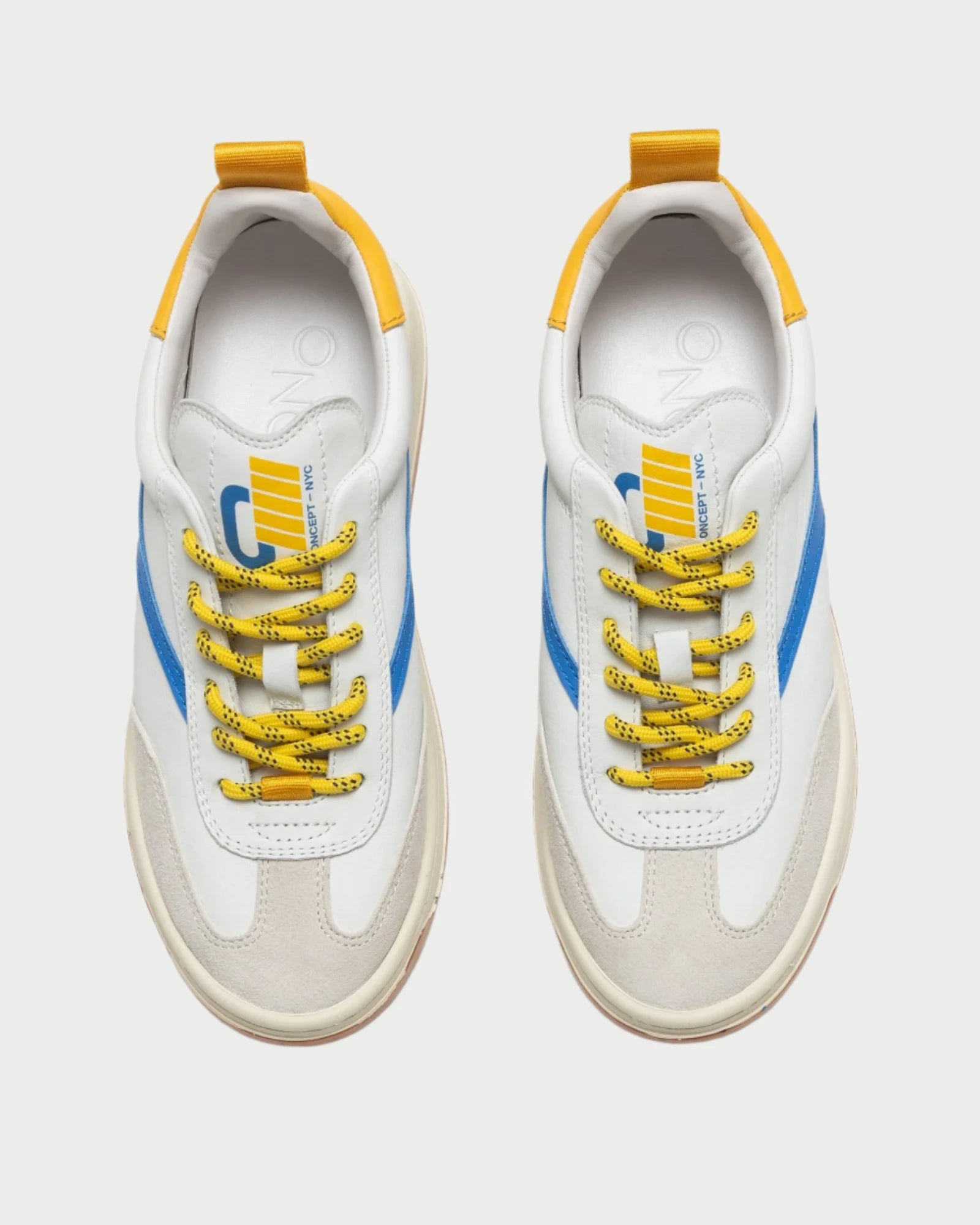 The Oncept Panama Shoe showcases a stylish design with white and beige uppers, complemented by blue side stripes and yellow accents, making it perfect for both turf and street. From a top-down view on a plain background, the sneakers exhibit unique yellow and black patterned laces.